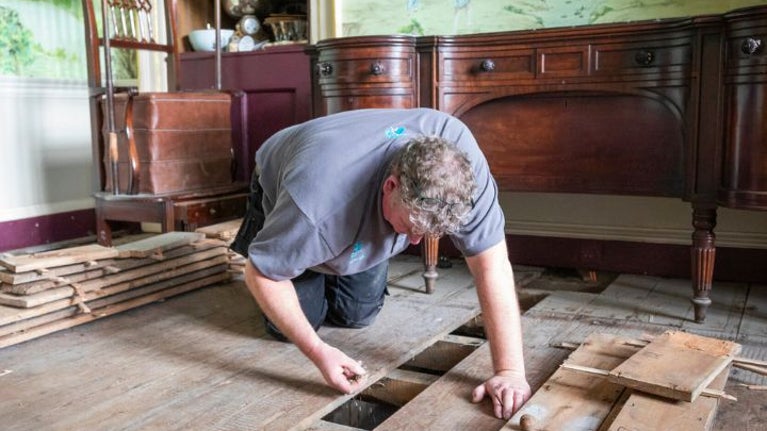 A member of the National Trust Specialist Crafts team inspecting flood damage under floorboards in the dining room of Avebury Manor.